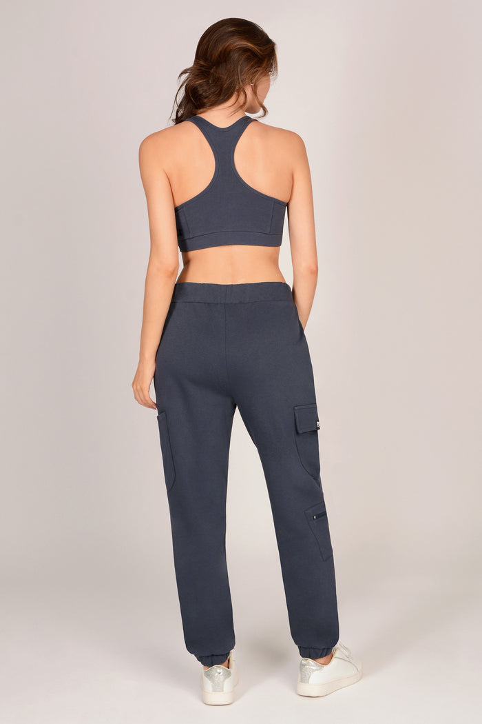 Woman wearing dark grey sports bra and matching combat joggers with pockets against a grey background.