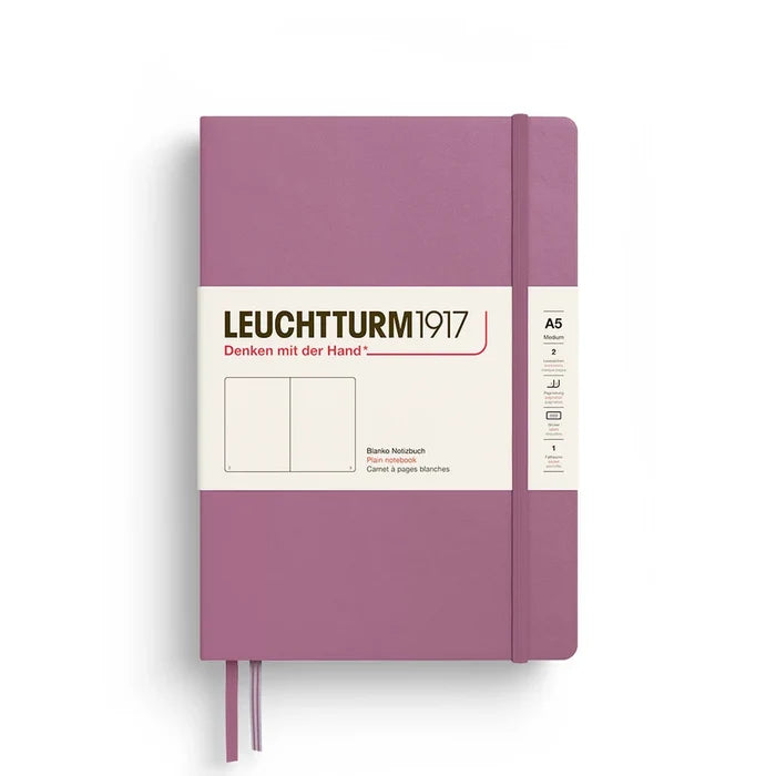 A Leuchtturm1917 A5 hardcover notebook in a dusty rose color, featuring a white paper label wrapped around the front and a matching purple ribbon bookmark hanging from the bottom.