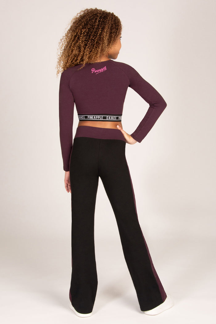Girl wearing a maroon brown long-sleeve crop top and matching black flared trousers on a plain background