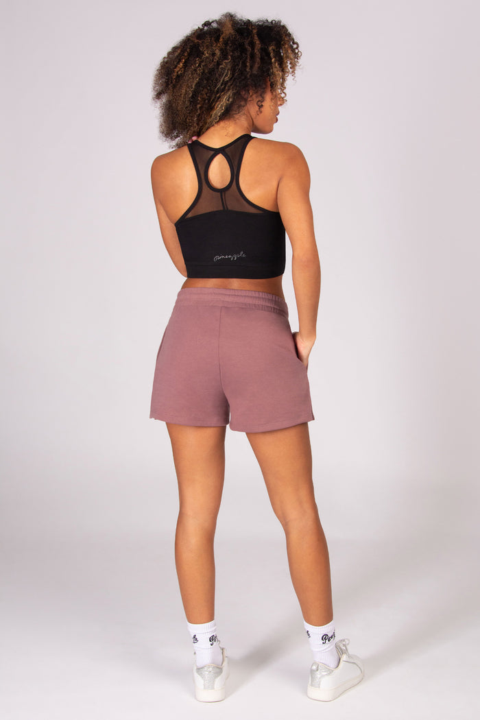 Woman wearing a black sports bra and sporty light brown shorts on a white background