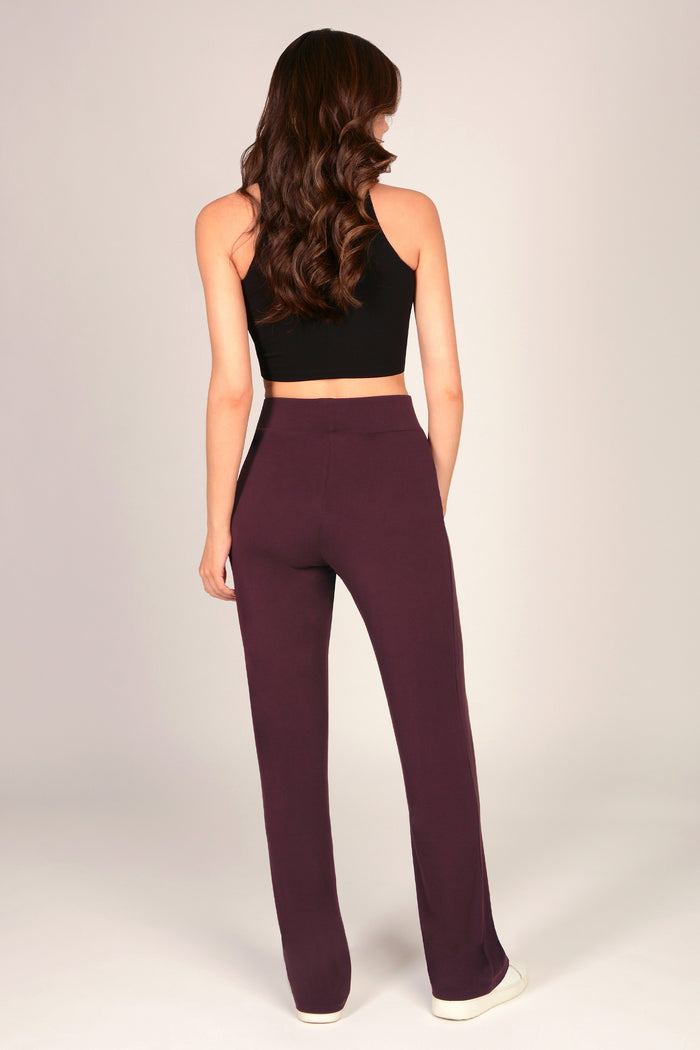 Woman wearing a black sleeveless crop top and maroon brown viscose trousers on a plain background