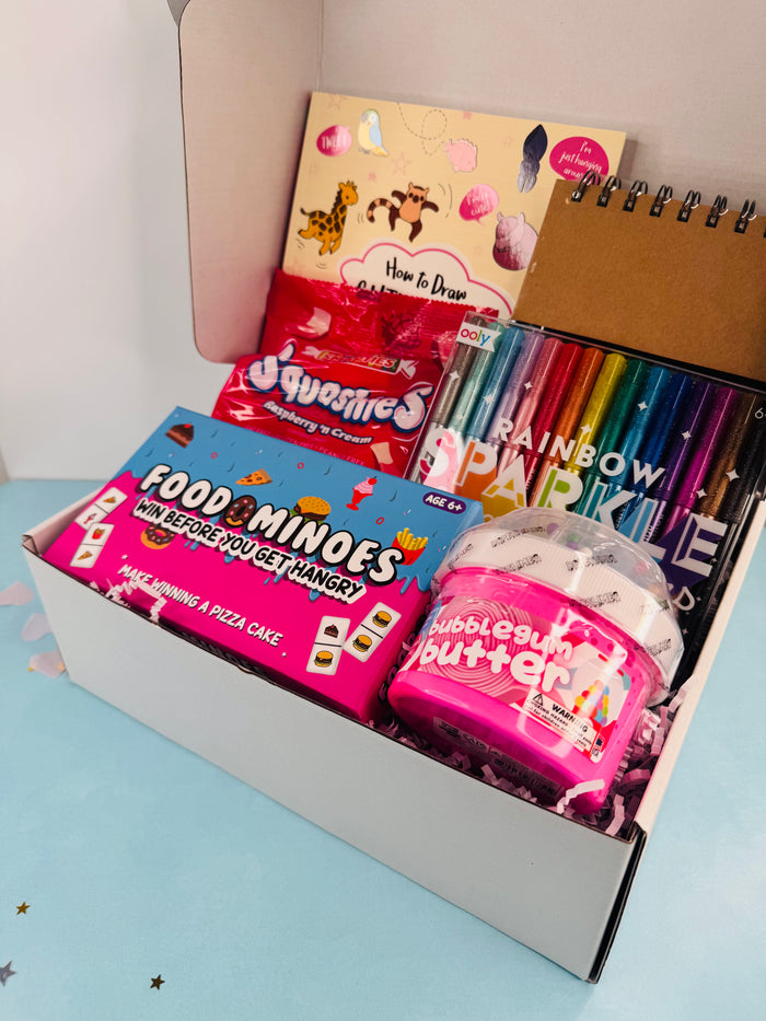 Open box containing various items including a notebook, candy, and a toy, on a light blue surface.