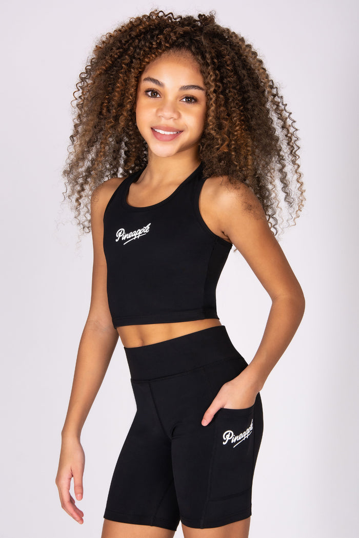 Girl wearing a black sports outfit with 'Pineapple' branding on a white background