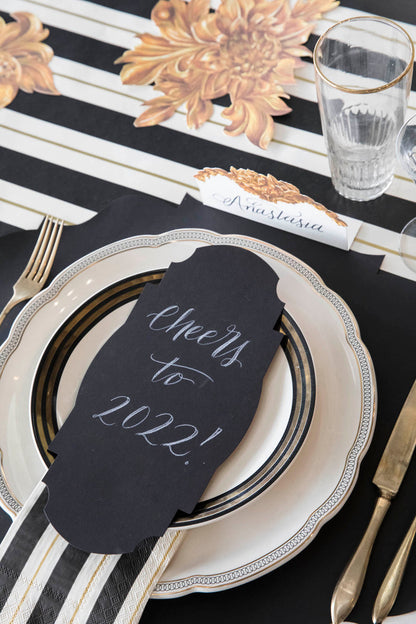 An elegant New Year's Even place setting with a Black Frame Table Accent resting on the plate with "Cheers to 2022!" hand-written in white script.