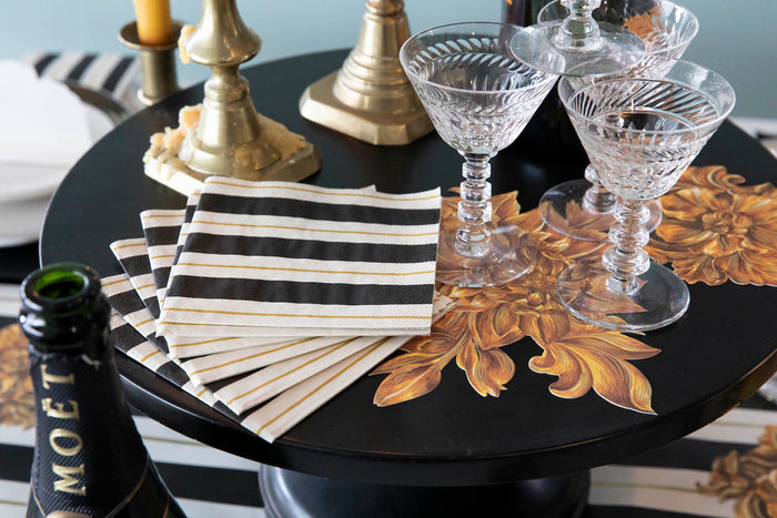 A stack of Black & Gold Awning Stripe Cocktail Napkins fanned out on an elegant tablescape.