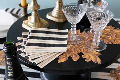 A stack of Black & Gold Awning Stripe Cocktail Napkins fanned out on an elegant tablescape.