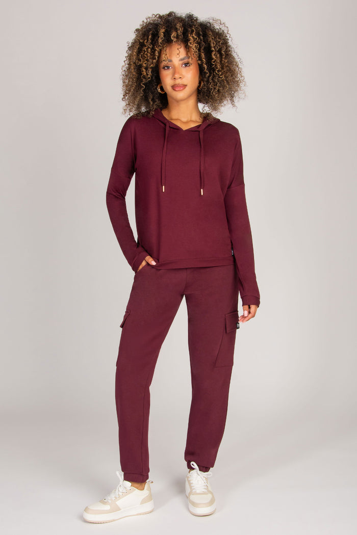 Woman wearing a burgundy tracksuit on a light gray background