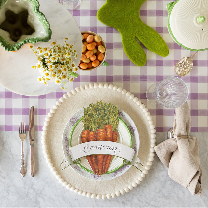 Easter table setting with the Ivory Felt Pom Pom Placemat, decorative plates, Carrots & Moss Classic Banner Table Accents on the Lilac Painted Check Runner.