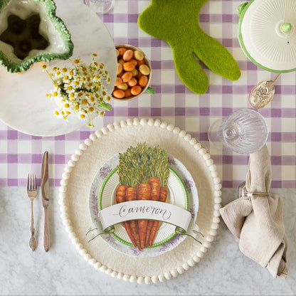 Easter table setting with the Ivory Felt Pom Pom Placemat, decorative plates, Carrots & Moss Classic Banner Table Accents on the Lilac Painted Check Runner.