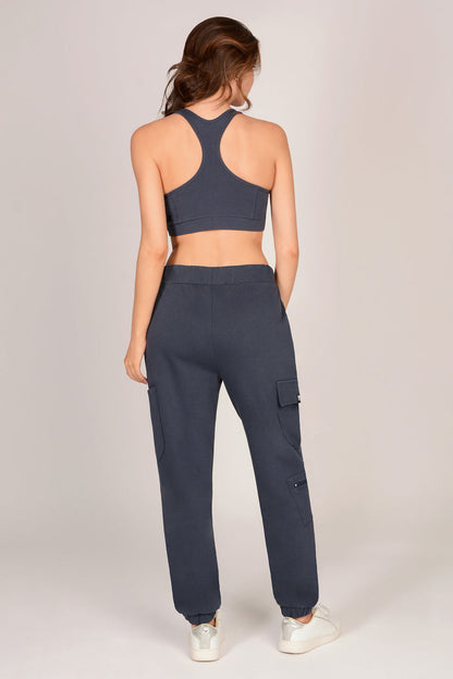 Woman wearing dark grey sports bra and matching combat joggers with pockets against a grey background.