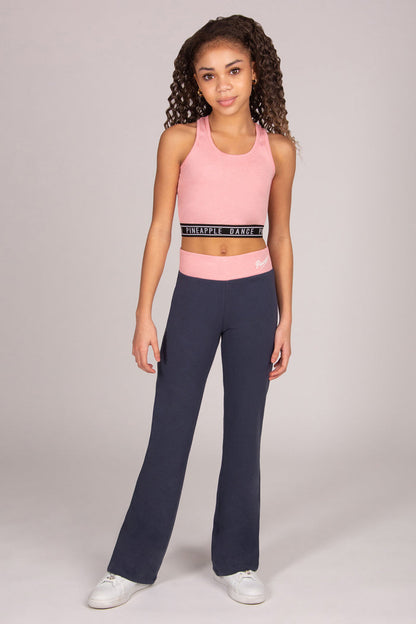 Girl wearing light pink sports crop top with matching dark grey bootcut trousers on plain background.