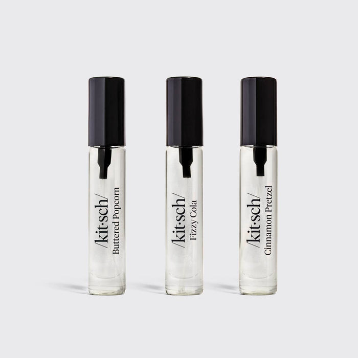 Three clear glass roll-on perfume bottles with black caps, labeled Kit's Cheddar Buttered Popcorn, Kit's Cheddar Fizzy Cola, and Kit's Cheddar Cinnamon Pretzel, arranged on a light gray background.