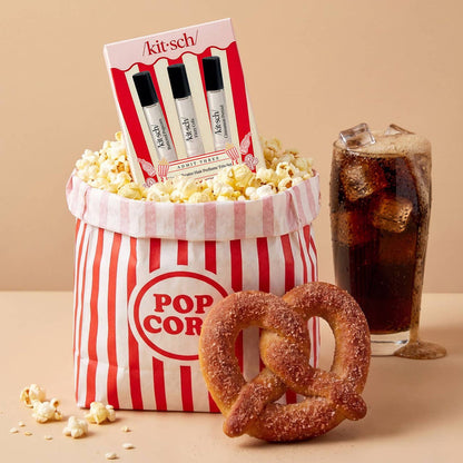 Popcorn bucket with popcorn, a glass of soda, and a pretzel on a beige background
