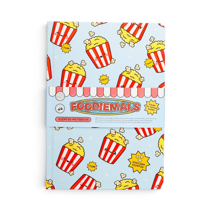 A Foodiemals scented notebook with a light blue cover decorated with a cartoon popcorn bucket pattern, wrapped in a pink and white striped paper band with the brand name 'FOODIEMALS' printed on it.