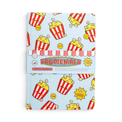A Foodiemals scented notebook with a light blue cover decorated with a cartoon popcorn bucket pattern, wrapped in a pink and white striped paper band with the brand name 'FOODIEMALS' printed on it.