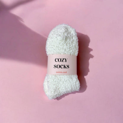 White fluffy sock with 'Cozy Socks' label on a pink background