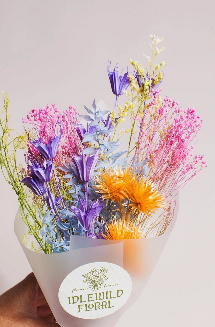 Bouquet of colorful flowers in a white container with 'Idlewild Floral' label on a light gray background
