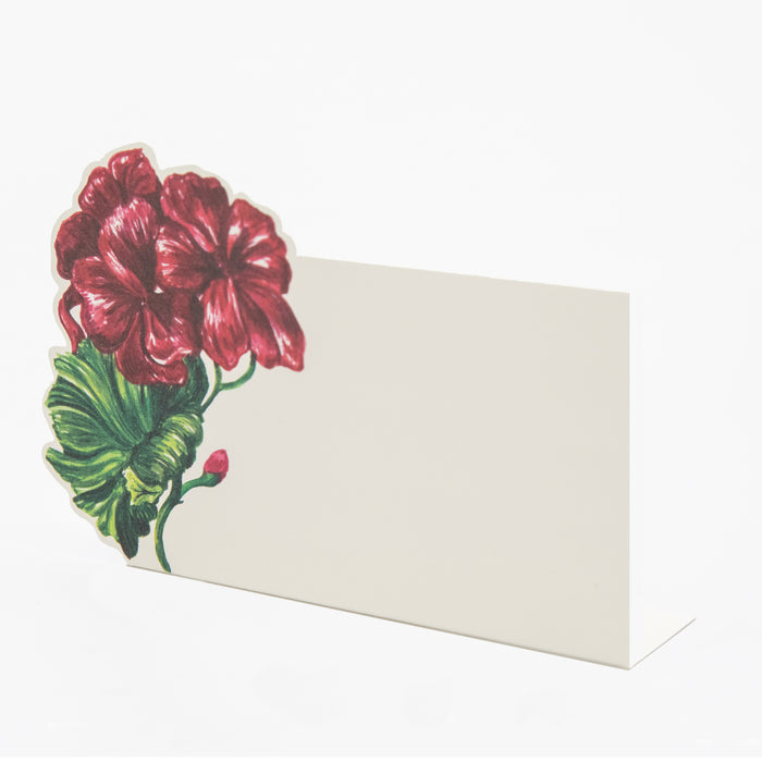 A white, rectangular freestanding place card featuring illustrated deep red geranium blooms with green foliage adorning the left edge of the card.