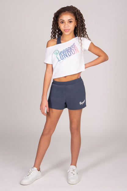 Girl wearing a white crop top with dark grey shorts on a light grey background