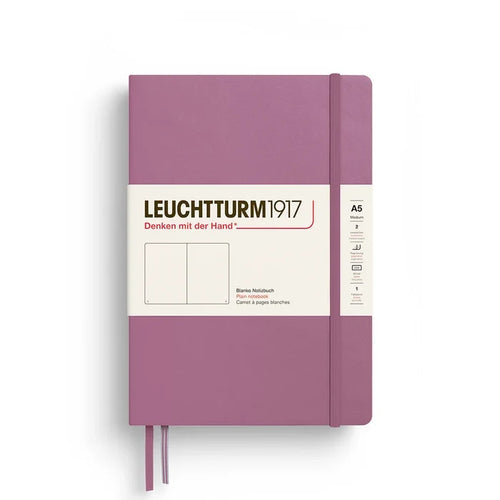 A Leuchtturm1917 A5 hardcover notebook in a dusty rose color, featuring a white paper label wrapped around the front and a matching purple ribbon bookmark hanging from the bottom.