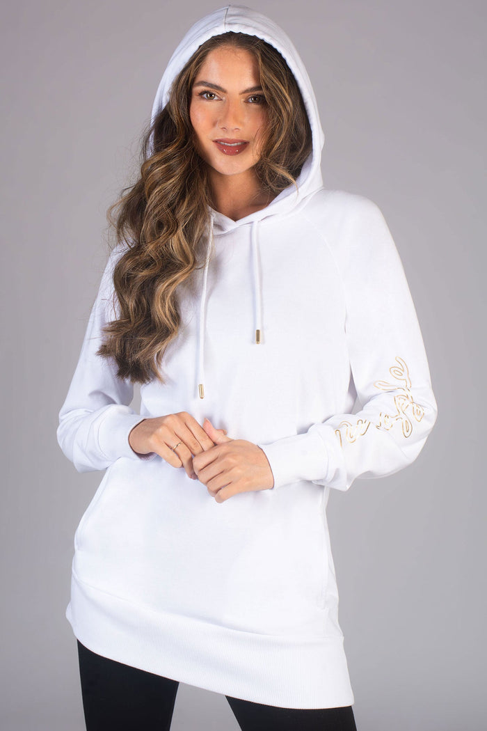 A woman wearing a white longline hoodie with a hood, featuring a drawcord, ribbed cuffs, and a gold Pineapple logo print along the left sleeve.