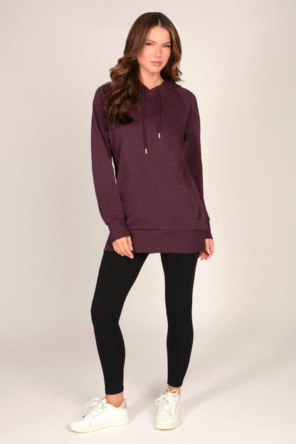 Woman wearing a maroon brown hoodie with black leggings against a grey background