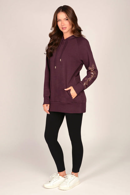 Woman wearing a maroon brown hoodie with pockets and black leggings against a grey background