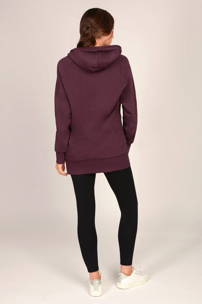 Woman wearing a maroon brown hoodie with black leggings against a grey background
