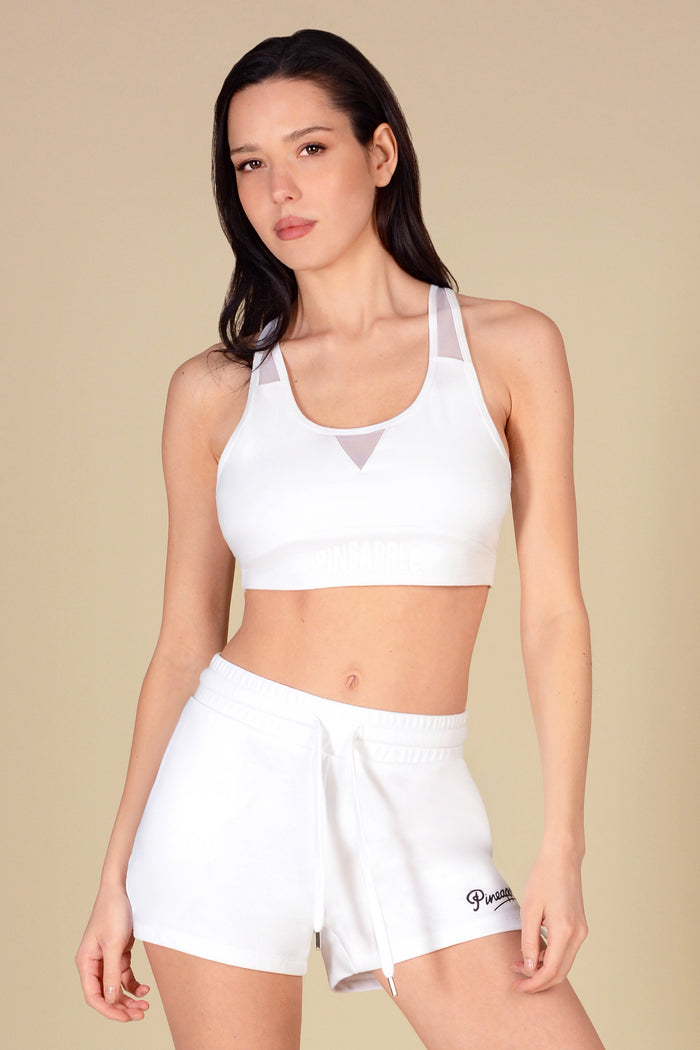 Woman wearing a white sports bra and shorts on a beige background