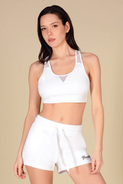Woman wearing a white sports bra and shorts on a beige background