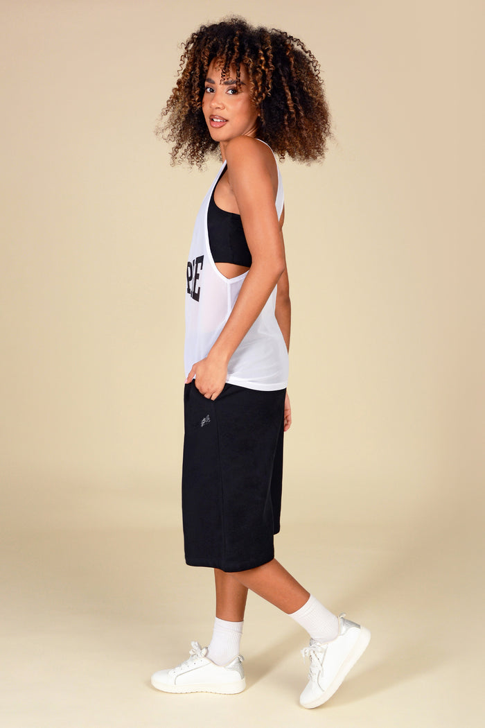 Woman wearing a white mesh vest and black shorts on a beige background