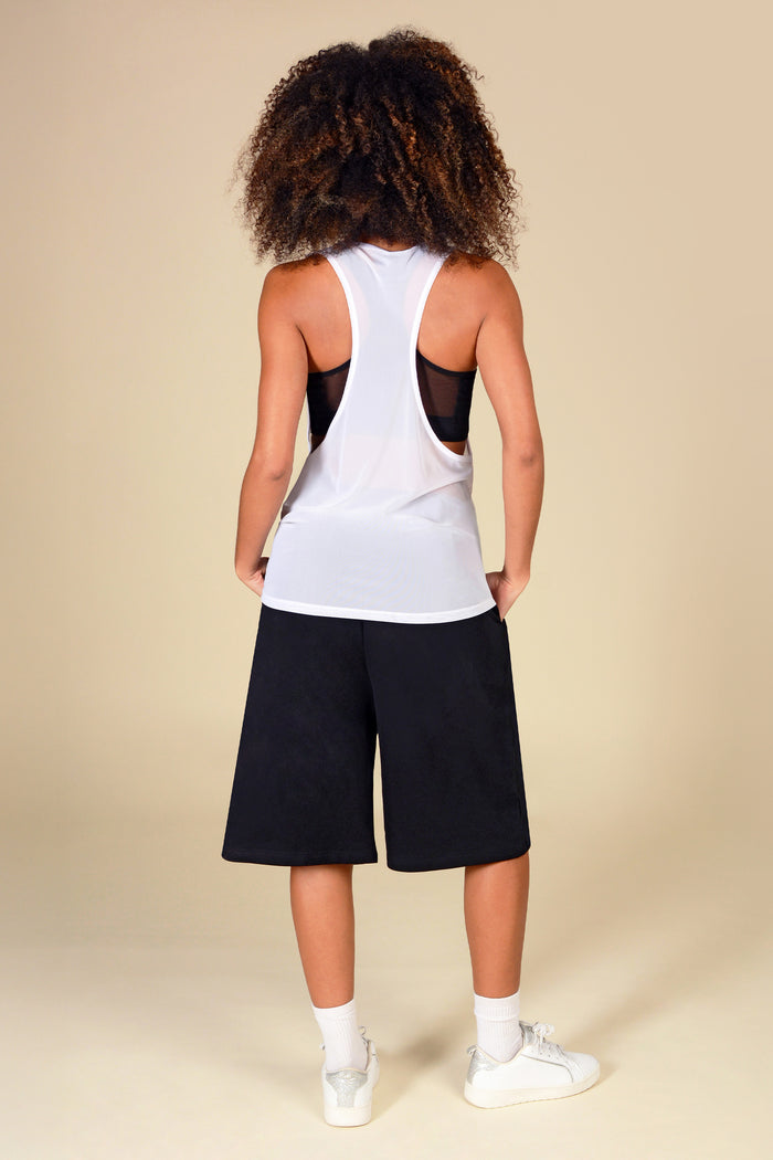 Woman wearing a white mesh vest with mesh panels and black shorts on a beige background