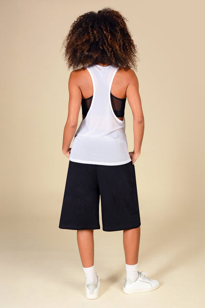 Woman wearing a white mesh vest with mesh panels and black shorts on a beige background