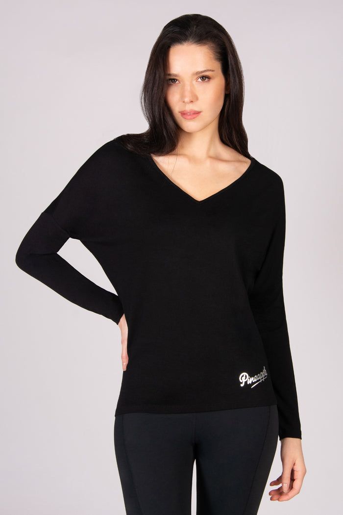 Woman wearing a black v-neckline long sleeve top on a grey background