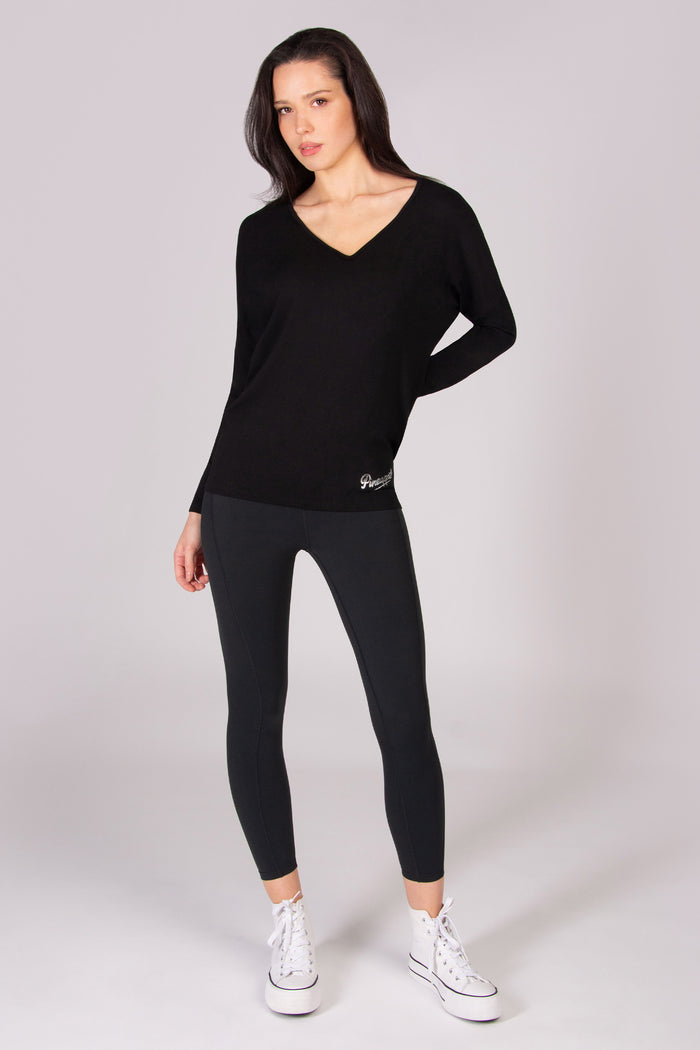 Woman wearing a black long-sleeve top with v neckline and leggings on a white background