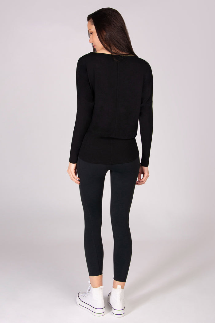 Woman wearing a black long-sleeve top and leggings on a white background