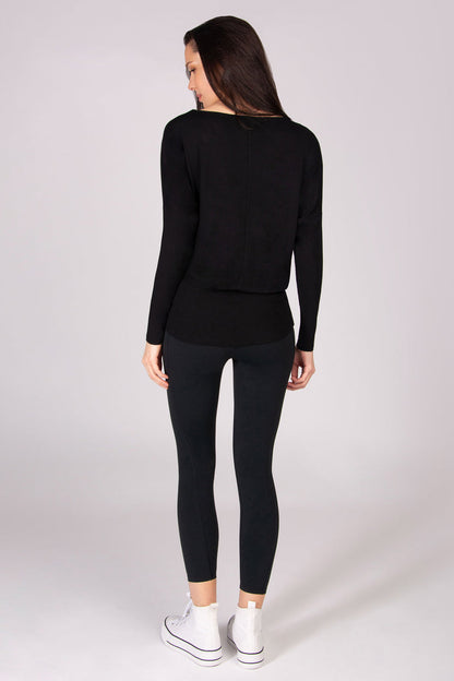Woman wearing a black long-sleeve top and leggings on a white background