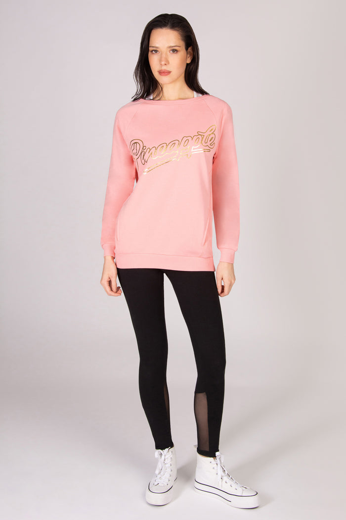 Woman wearing a coral pink oversized sweatshirt, black leggings, and white sneakers on a white background