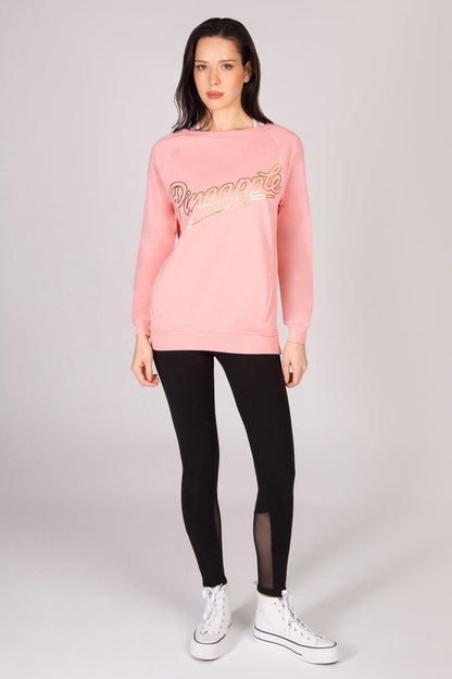 Woman wearing a coral pink oversized sweatshirt, black leggings, and white sneakers on a white background