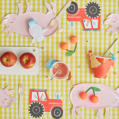 A yellow and white gingham table top with various farm-inspired party decor, including truck-shaped paper napkins and pig-shaped paper plates.