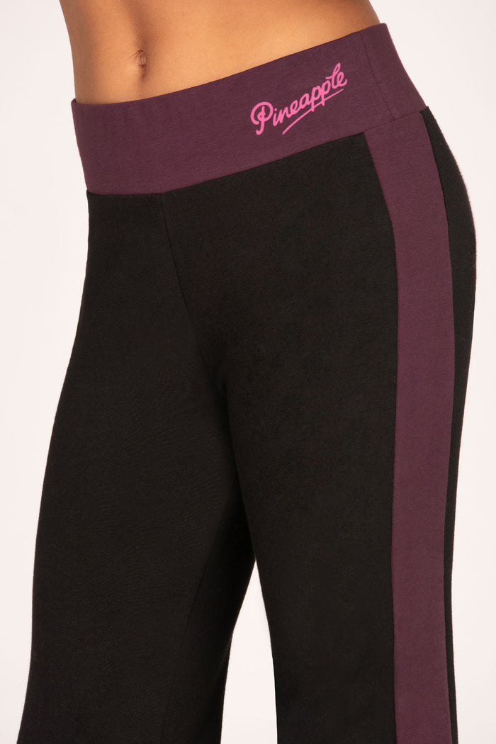 Black flared trousers with a maroon brown waistband and side stripe featuring 'Pineapple' branding.