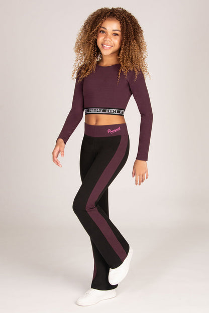 Girl wearing a maroon brown long-sleeve crop top and matching black flared trousers on a plain background