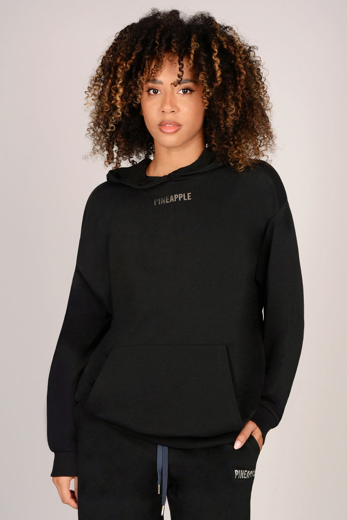 Woman wearing a black hoodie with 'Pineapple' branding on a plain background