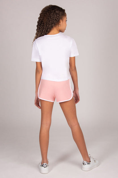 Young girl wearing a white t-shirt and light pink shorts on a light grey background
