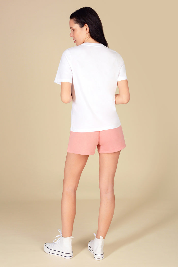 Woman wearing a regular fit white t-shirt with light pink sporty shorts against a light yellow background.