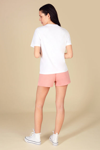 Woman wearing a regular fit white t-shirt with light pink sporty shorts against a light yellow background.