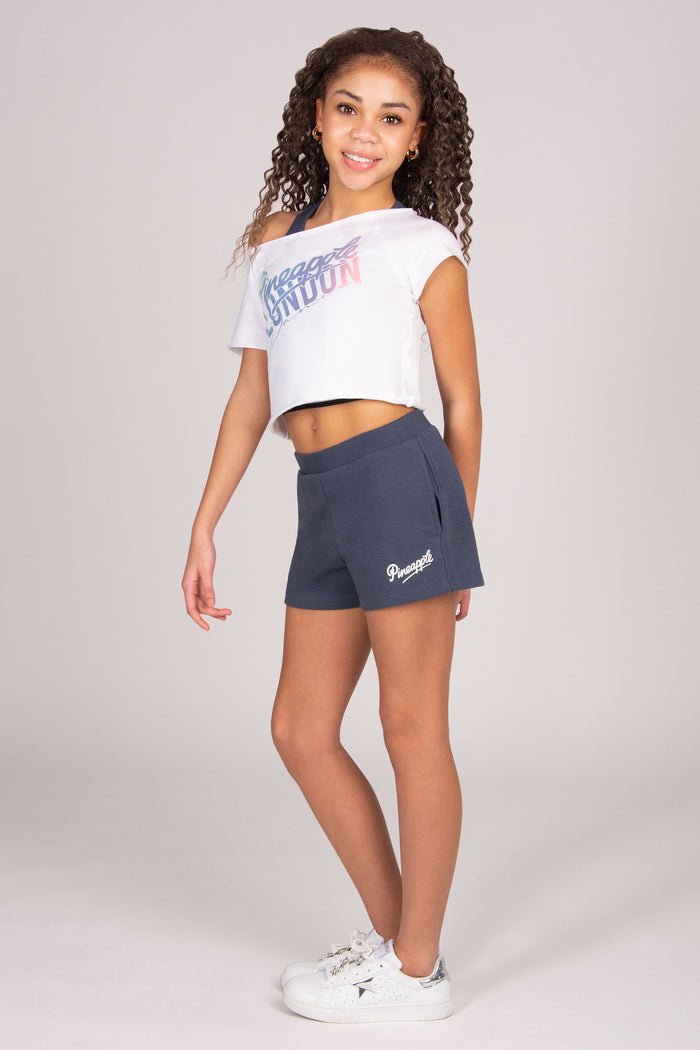 Girl wearing a white crop top and dark grey pocket shorts on a plain background