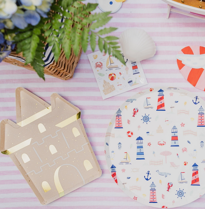 Decorative items including a castle-shaped card and a plate with lighthouse pattern on a pink striped background.