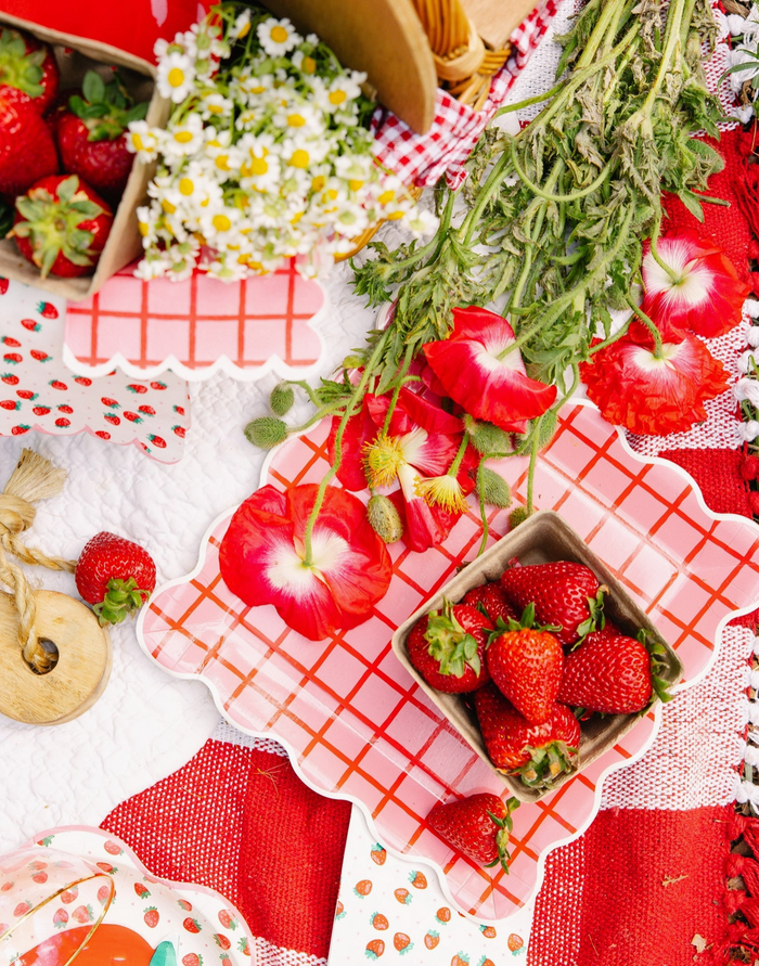 Strawberries and flowers on a red checkered tablecloth with a decorative plate.