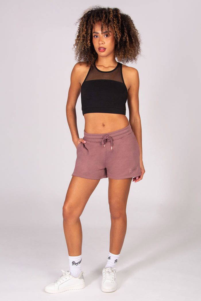 Woman wearing a black sports bra and light brown sporty shorts on a white background